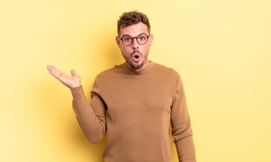 Genç, yakışıklı İspanyol bir adam şaşırmış ve şok olmuş görünüyor, çenesi düşmüş, elinde açık bir elle bir nesne tutuyor.