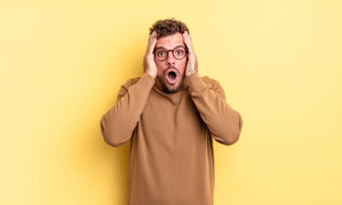 Genç, yakışıklı, İspanyol görünümlü, hoş olmayan, korkmuş ya da endişeli, ağzı açık ve iki kulağını da elleriyle kapatan bir adam.