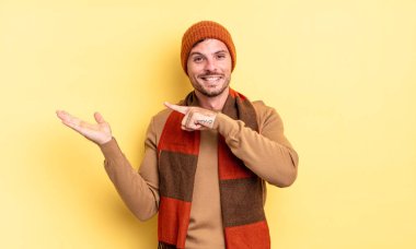 Genç, yakışıklı İspanyol adam neşeyle gülümsüyor ve yan taraftaki fotokopi alanını işaret ederek bir nesneyi gösteriyor ya da reklamını yapıyor.