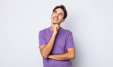 Genç, yakışıklı İspanyol adam mutlu bir şekilde gülümsüyor ve hayal kuruyor ya da şüphe ediyor.