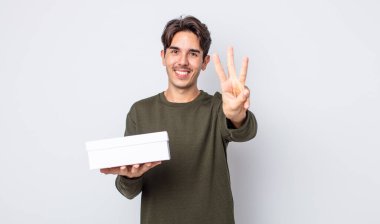 Genç İspanyol adam gülümsüyor ve arkadaş canlısı görünüyor, üç numarayı gösteriyor. beyaz kutu kavramı