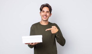 Genç İspanyol adam neşeyle gülümsüyor, mutlu hissediyor ve bir tarafı işaret ediyor. beyaz kutu kavramı