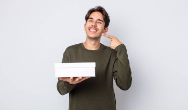 Genç İspanyol adam kendine güvenerek gülümsüyor ve kendi gülüşünü gösteriyor. beyaz kutu kavramı