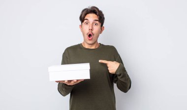 Genç İspanyol bir adam şok olmuş ve ağzı açık, kendini işaret ederek şaşırmış görünüyor. beyaz kutu kavramı