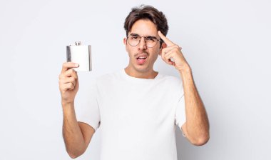 Genç İspanyol adam şaşkın ve şaşkın hissediyor, senin deli olduğunu gösteriyor. alkol şişesi konsepti