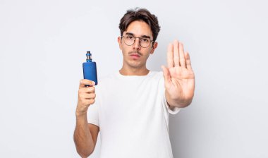 Genç İspanyol adam ciddi görünüyor. Avuç içi gösteriyor. Durdurma hareketi yapıyor. duman buharlaştırıcı kavramı