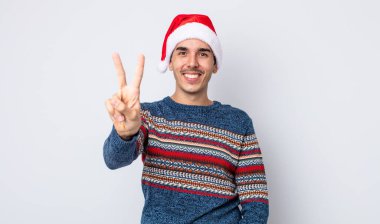 Genç İspanyol adam gülümsüyor ve arkadaş canlısı görünüyor, iki numarayı gösteriyor. Yeni yıl ve Noel konsepti
