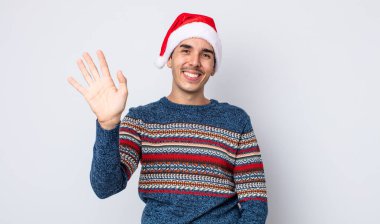 Genç İspanyol adam mutlu bir şekilde gülümsüyor, el sallıyor, sizi selamlıyor ve selamlıyor. Yeni yıl ve Noel konsepti