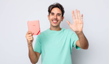 Genç İspanyol adam mutlu bir şekilde gülümsüyor, el sallıyor, sizi selamlıyor ve selamlıyor. 2022 planlayıcı kavramı