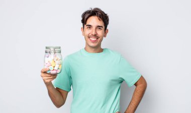 Genç İspanyol adam mutlu bir şekilde gülümsüyor, eli kalçasında ve kendinden emin. jöle şekeri konsepti