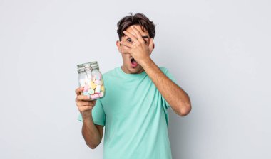 Genç İspanyol bir adam şok olmuş, korkmuş ya da korkmuş görünüyor. Yüzü elle kapatılmış. jöle şekeri konsepti