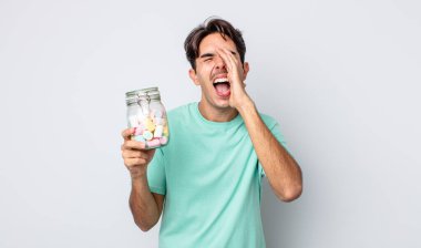 Genç İspanyol adam kendini mutlu hissediyor, elleri ağızının yanında bağırarak bağırıyor. jöle şekeri konsepti