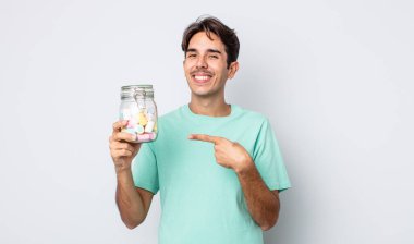 Genç İspanyol adam neşeyle gülümsüyor, mutlu hissediyor ve bir tarafı işaret ediyor. jöle şekeri konsepti