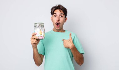 Genç İspanyol bir adam şok olmuş ve ağzı açık, kendini işaret ederek şaşırmış görünüyor. jöle şekeri konsepti