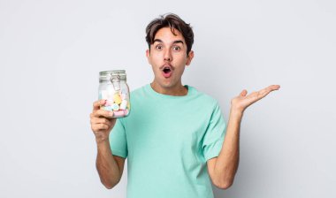 Genç İspanyol bir adam şaşırmış ve şok olmuş görünüyor. Çenesi düşmüş ve elinde bir nesne tutuyor. jöle şekeri konsepti