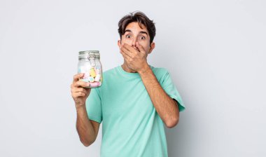 Genç İspanyol adam şok olmuş bir şekilde ağzını eliyle kapatıyor. jöle şekeri konsepti