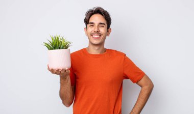 Genç İspanyol adam mutlu bir şekilde gülümsüyor, eli kalçasında ve kendinden emin. dekoratif bitki konsepti