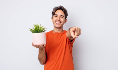 Genç İspanyol adam kamerayı göstererek seni seçiyor. dekoratif bitki konsepti