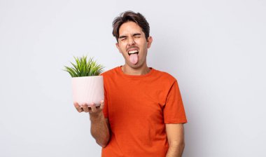 Neşeli ve asi tavırlı, şaka yapan ve dilini dışarı çıkaran genç İspanyol bir adam. dekoratif bitki konsepti