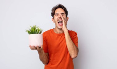 Genç İspanyol adam kendini mutlu hissediyor, elleri ağızının yanında bağırarak bağırıyor. dekoratif bitki konsepti
