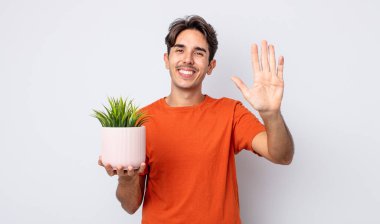 Genç İspanyol adam mutlu bir şekilde gülümsüyor, el sallıyor, sizi selamlıyor ve selamlıyor. dekoratif bitki konsepti