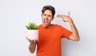 Genç İspanyol adam mutsuz ve stresli görünüyor, intihar jesti silah işareti yapıyor. dekoratif bitki konsepti