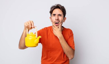 Ağzı ve gözleri sonuna kadar açık ve eli çenesinde genç İspanyol bir adam. çaydanlık konsepti