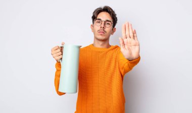 Genç İspanyol adam ciddi görünüyor. Avuç içi gösteriyor. Durdurma hareketi yapıyor. termos kavramı
