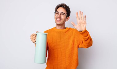 Genç İspanyol adam mutlu bir şekilde gülümsüyor, el sallıyor, sizi selamlıyor ve selamlıyor. termos kavramı