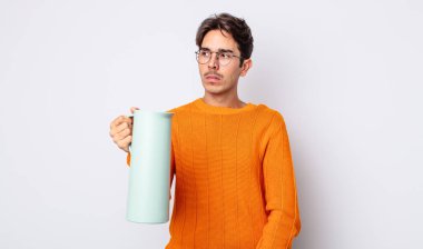 Genç İspanyol bir adam üzgün, üzgün ya da kızgın hissediyor ve yan tarafa bakıyor. termos kavramı