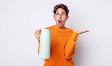 Genç İspanyol bir adam şaşırmış ve şok olmuş görünüyor. Çenesi düşmüş ve elinde bir nesne tutuyor. termos kavramı