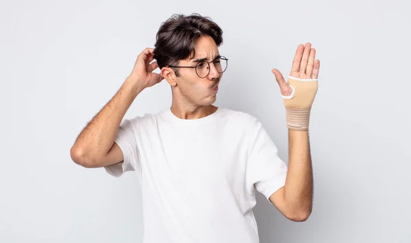 Young Hispanic Man Feeling Puzzled Confused Scratching Head Hand Bandage — Stock Photo, Image