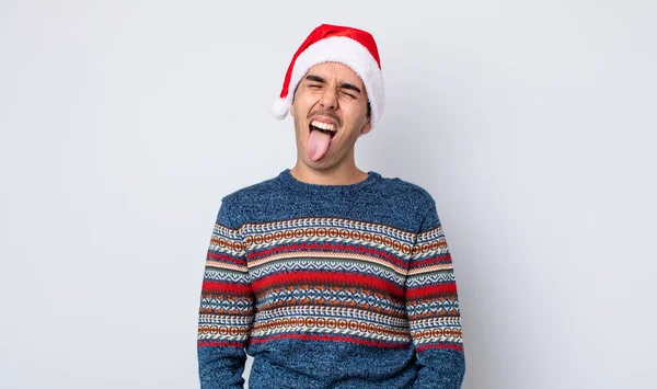 陽気で反抗的な態度を持つ若いヒスパニック系の男冗談と舌を突き出す 新年とクリスマスのコンセプト — ストック写真