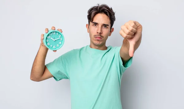 若いヒスパニック系の男がクロスを感じ親指を下に示す 目覚まし時計のコンセプト — ストック写真