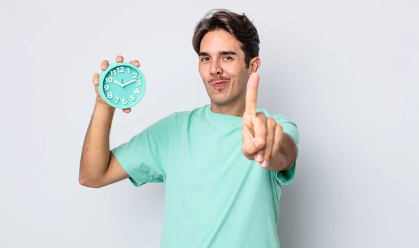 若いヒスパニック系の男は誇らしげに笑顔と自信を持ってナンバーワンを作ります 目覚まし時計のコンセプト — ストック写真