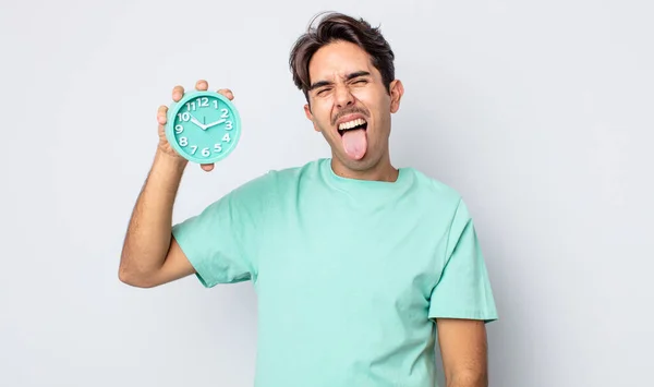 陽気で反抗的な態度を持つ若いヒスパニック系の男冗談と舌を突き出す 目覚まし時計のコンセプト — ストック写真
