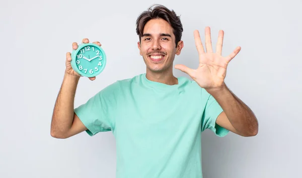 若いヒスパニック系の男は笑顔で友好的に見える 5番を示しています 目覚まし時計のコンセプト — ストック写真