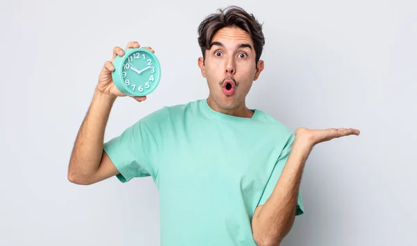 若いヒスパニック系の男が驚いてショックを受け 顎が物を持って落下した 目覚まし時計のコンセプト — ストック写真