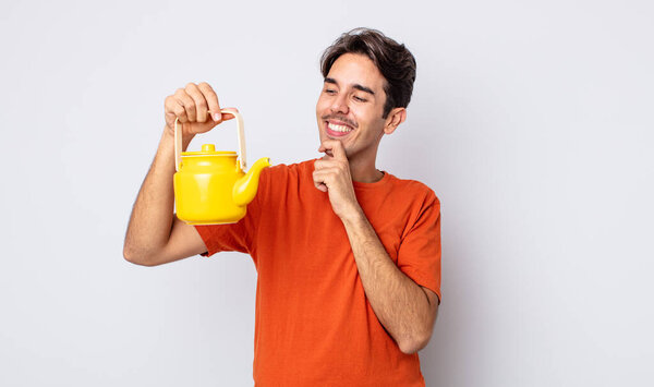 Молодой латиноамериканец улыбается со счастливым, уверенным выражением лица с рукой на подбородке. Концепция чайника