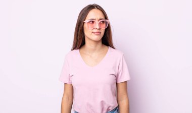 Genç, güzel bir kadın üzgün, üzgün ya da kızgın hissediyor ve yan tarafa bakıyor. pembe güneş gözlüğü konsepti