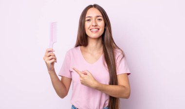 Genç, güzel bir kadın neşeyle gülümsüyor, mutlu hissediyor ve bir tarafı işaret ediyor. saç tarağı konsepti