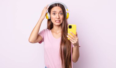 Genç ve güzel bir kadın gergin, endişeli ya da korkmuş hissediyor. Elleri başının üstünde. Kulaklık ve akıllı telefon.