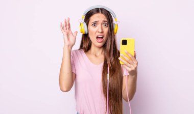 Genç ve güzel bir kadın ellerini havaya kaldırarak çığlık atıyor. Kulaklık ve akıllı telefon.