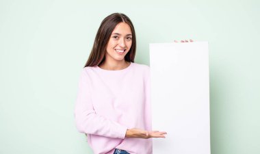 Genç, güzel bir kadın neşeyle gülümsüyor, mutlu hissediyor ve bir konsept gösteriyor. boş tuval kavramı