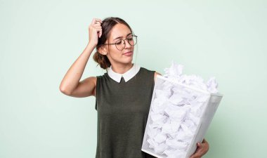 Genç ve güzel bir kadın mutlu bir şekilde gülümsüyor ve hayal kuruyor ya da şüphe ediyor. kağıt toplar çöp konsepti