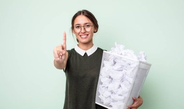 Genç, güzel bir bayan gülümsüyor ve arkadaş canlısı görünüyor. Bir numarayı gösteriyor. kağıt toplar çöp konsepti