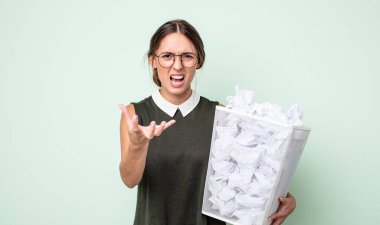 Genç ve güzel bir kadın sinirli, sinirli ve sinirli görünüyor. kağıt toplar çöp konsepti
