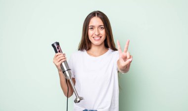 Genç, güzel bir bayan gülümsüyor ve iki numarayı gösteriyor. el karıştırıcı konsepti