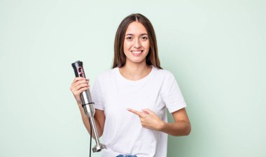 Genç, güzel bir kadın neşeyle gülümsüyor, mutlu hissediyor ve bir tarafı işaret ediyor. el karıştırıcı konsepti