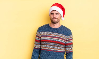 Genç ve yakışıklı bir adam üzgün, üzgün ya da kızgın hissediyor ve yan tarafa bakıyor. Noel konsepti
